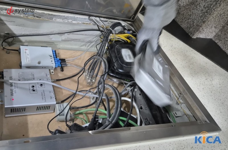 바닥 점검구 통신함 내부에 광 분배기와 통신 장비, 케이블이 모여 있고 장비 라벨은 모자이크 처리된 모습