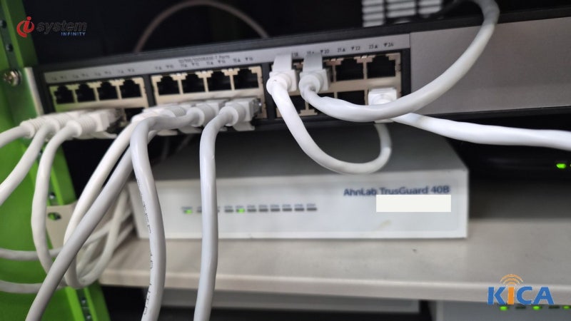 스위치 포트에 여러 가닥의 랜케이블이 꽂혀 있고 그 아래 선반에 AhnLab TrusGuard 40B 방화벽 장비가 놓인 클로즈업