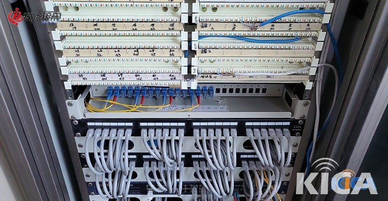 시흥 공장 통신실에 새로 구축된 Cat6A 패치패널과 네트워크 스위치 — 회색·노란색 패치코드로 용도별 분류된 깔끔한 정합 모습