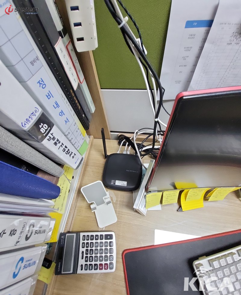 사무실 책상 위 검정 무선 라우터·USB 동글·노란 메모지·계산기 — 사무 업무 환경
